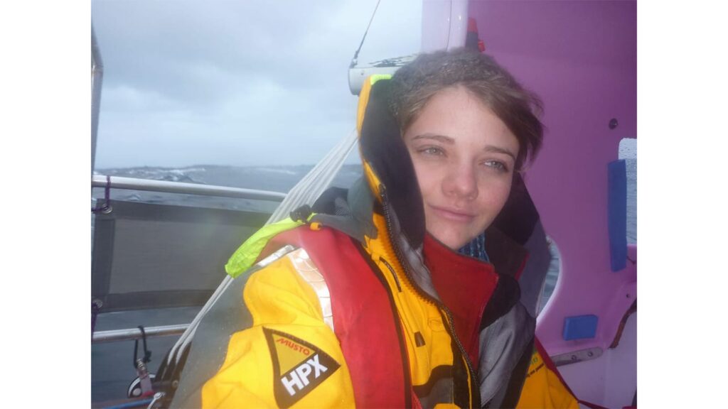 Jessica Watson smiling in sailing gear on deck with rigging visible behind her.