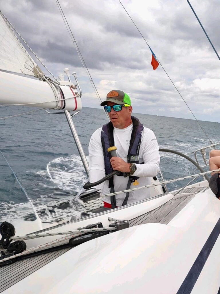 A man working the winch of a sailboat on a stormy day.