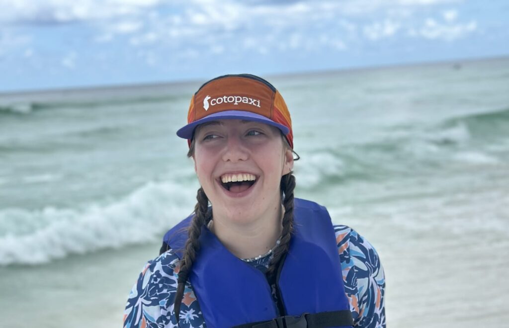 A smiling teen girl standing on a beach in a life jacket