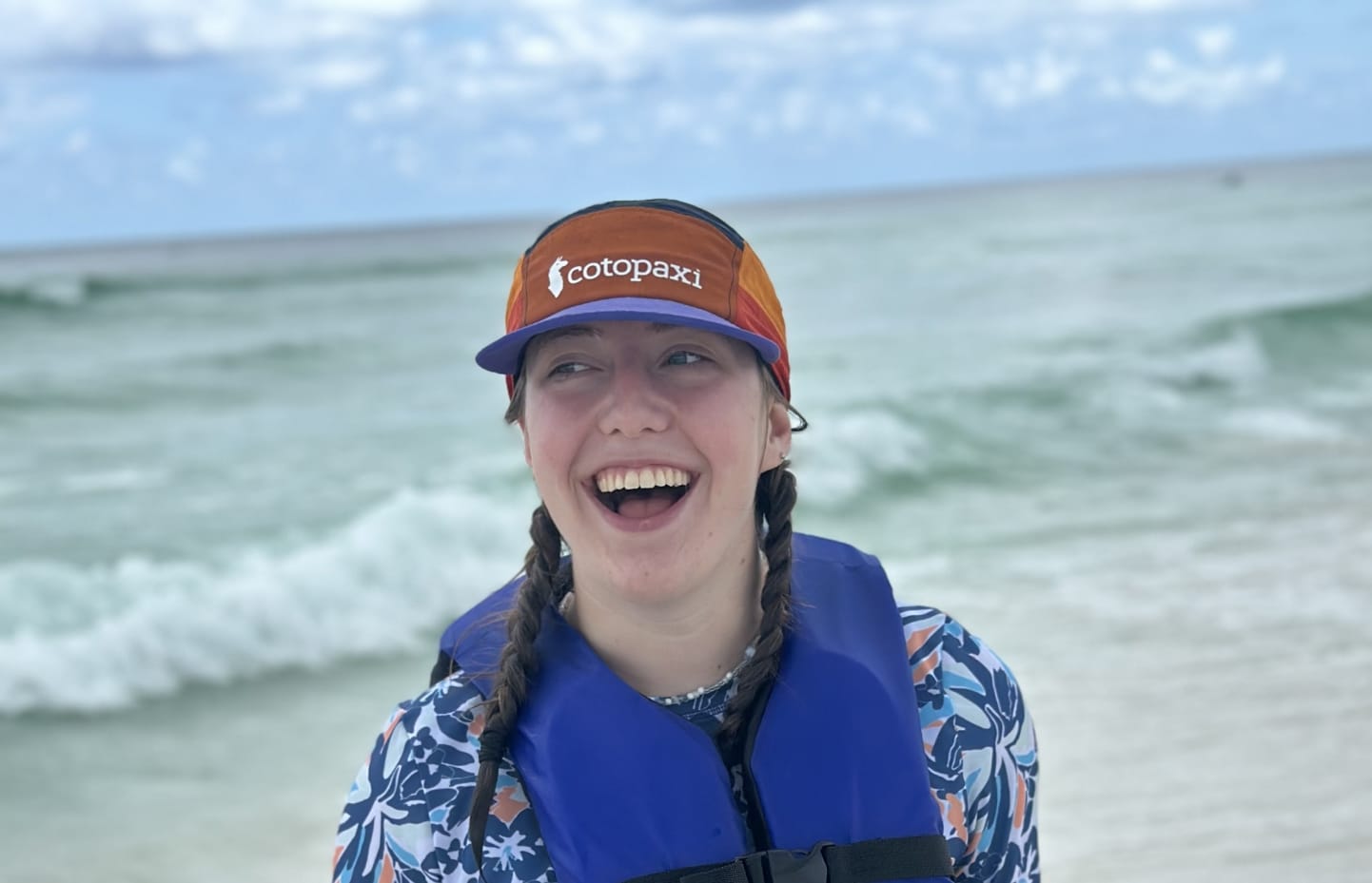 A smiling teen girl standing on a beach in a life jacket