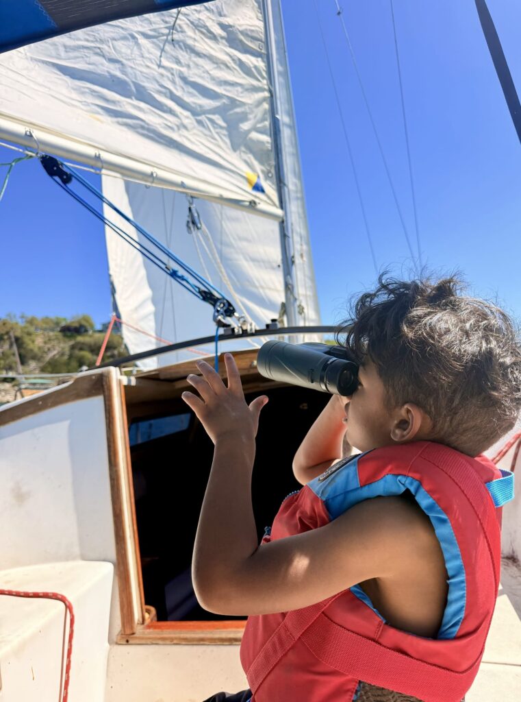 A boy looks through binoculars aboard a small sailboat