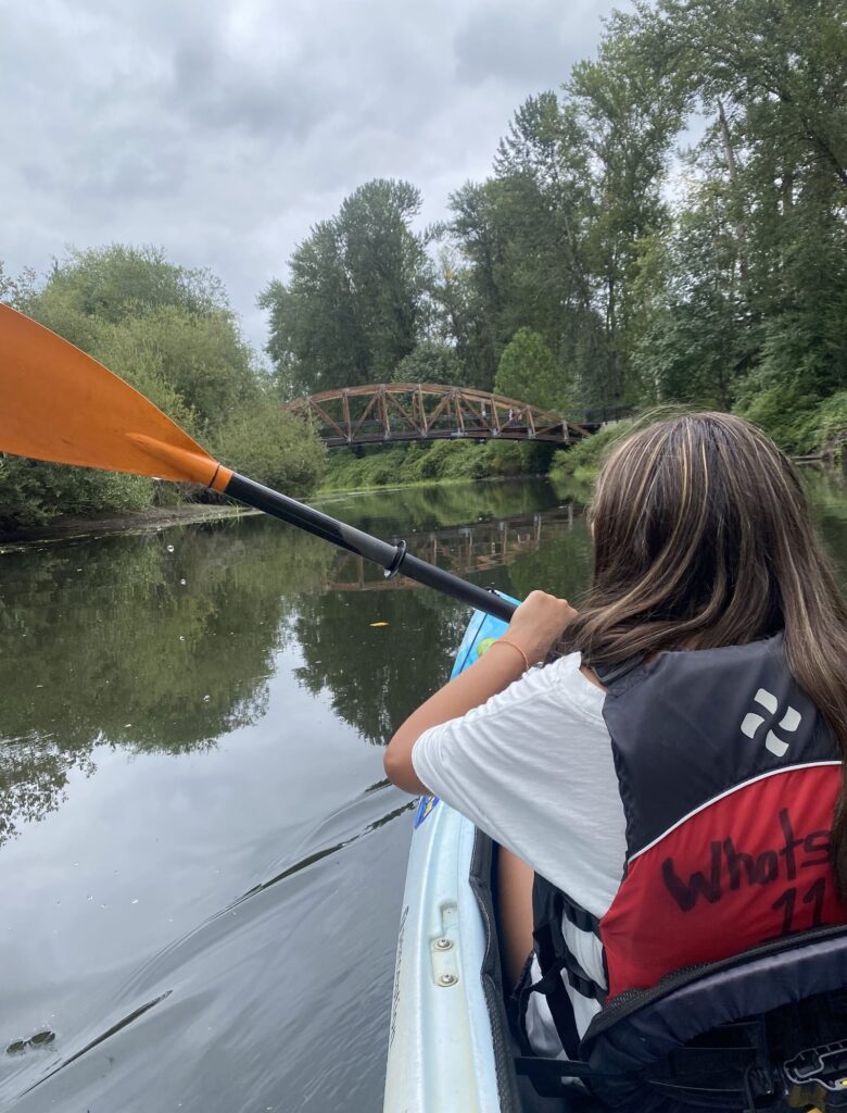 A view of a river, looking over a kayaker's shoulder.