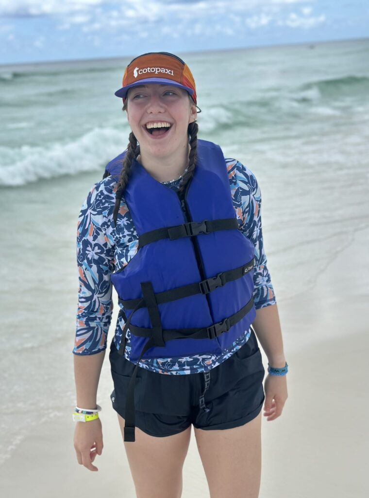 A teen wearing a life jacket on a beach