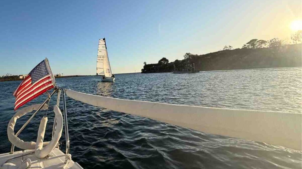 An American Flag flies off the back of a saiboat in a calm harbor.