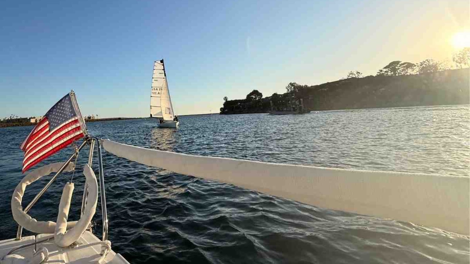 An American Flag flies off the back of a saiboat in a calm harbor.