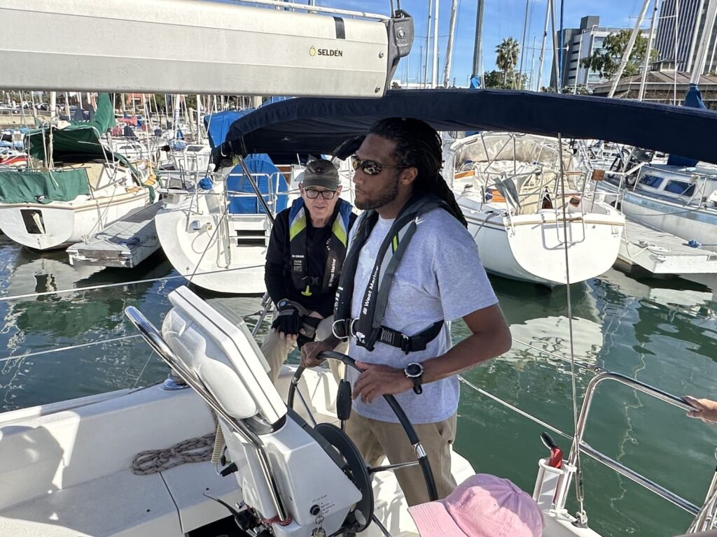a beginner sailor at the helm, under the watchful eye of a sailing instructor