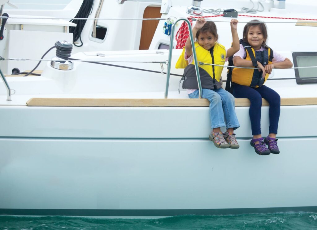 two young children sit on a sailboat with their feet hanging over the side