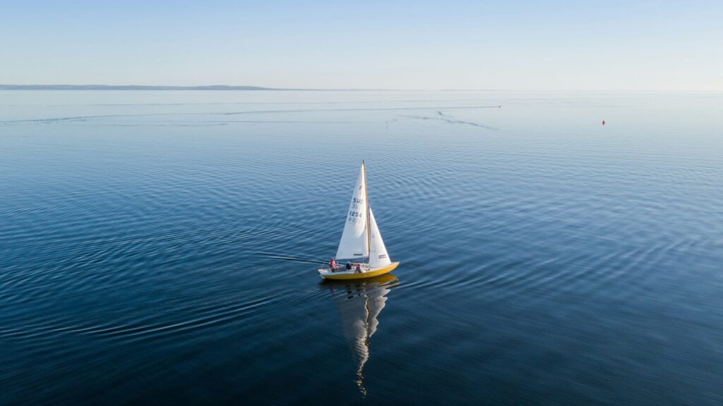 A sailboat seen from far above, surrounded by calm water