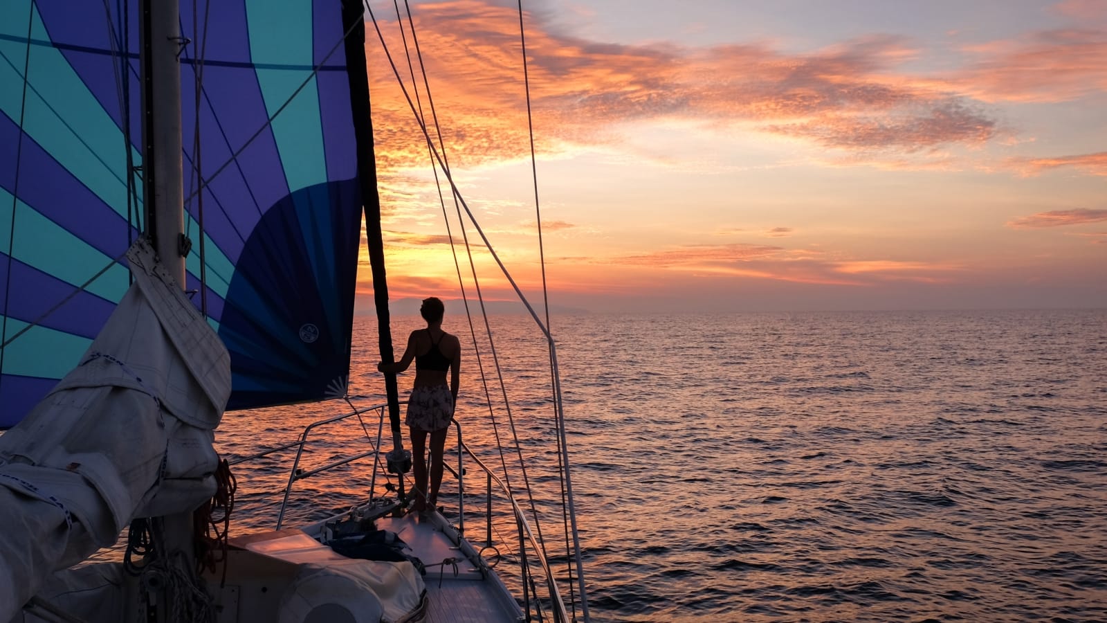 A woman silhouetted on a sailboat at sunset